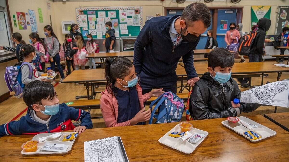 Principal Nate McGill helps settle Afghan students, from right Raihan, 6, Pakiza, 9, and Faizan, 8, as they eat breakfast on their first day back to at Ethel I. Baker Elementary School in Sacramento on Monday, Nov. 8, 2021. Afghan refugee students in Sacramento face language, trauma and school navigation barriers that increase dropout risk; community support and programs can help.